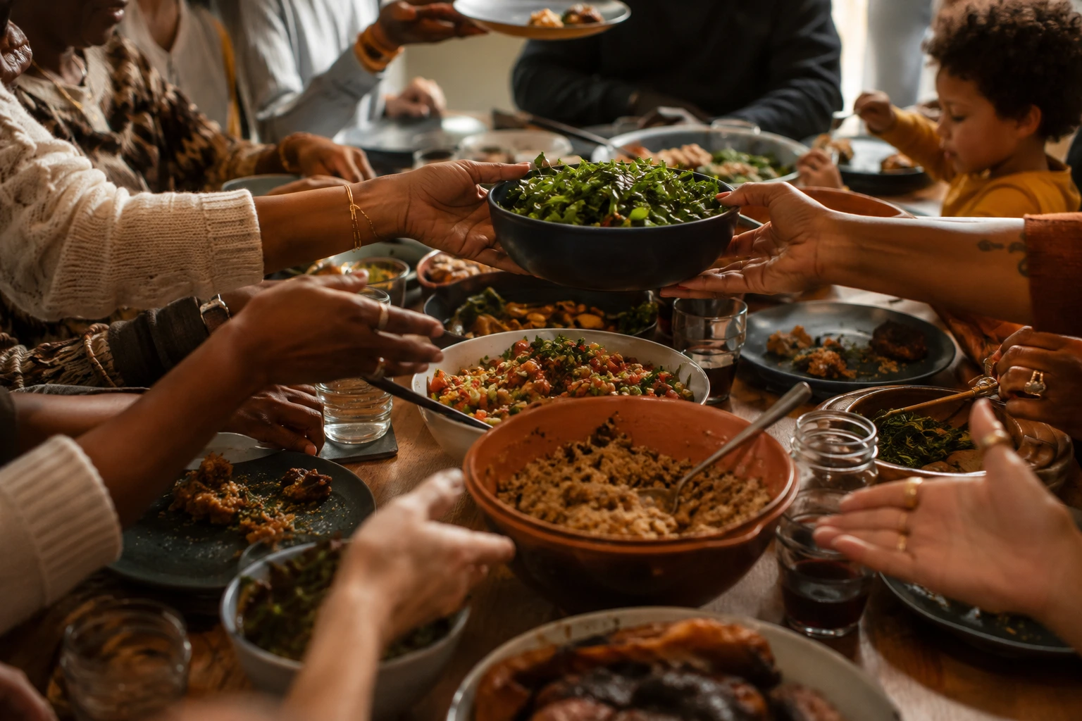 Many hands reaching in to pass dishes around a full communal table