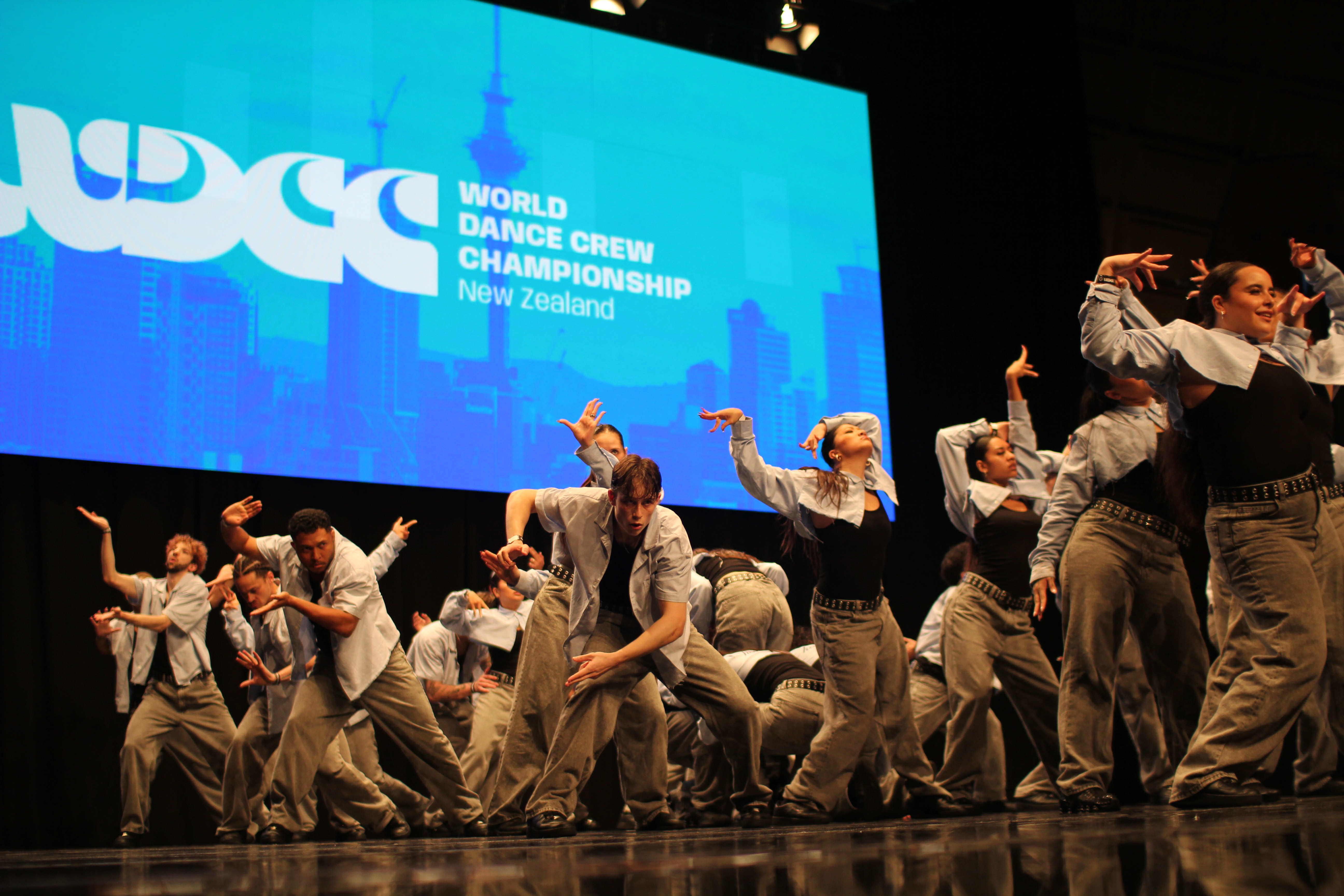 Crew performing at World Dance Crew Championship 2025 in front of the WDCC New Zealand screen